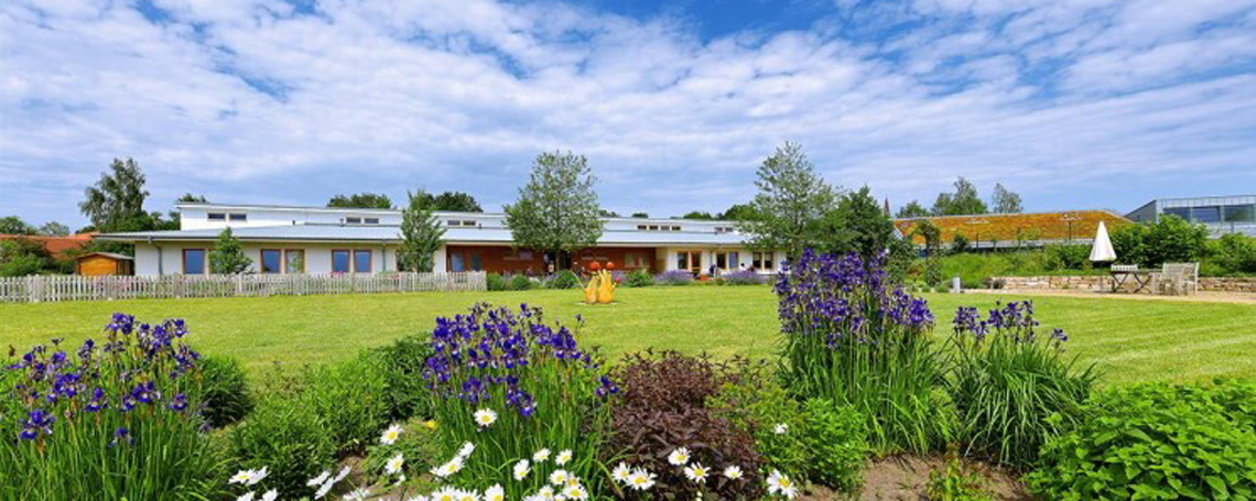 gebaeude_aussen_mitGarten_2025.jpg gebaeude_aussen_mitGarten_2025.jpg